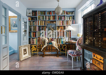 Blau lackierten Regalen in Bibliothek mit antiken Schaukelpferd und Cory Visitorian gepolsterten Stuhl Stockfoto