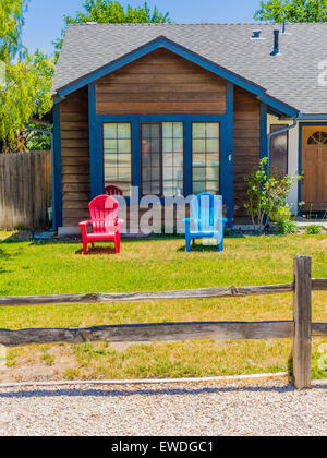 Zwei bunten Liegestühlen, einem roten und das andere blau, stehen auf dem Rasen eines Holzhauses. Stockfoto