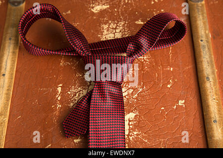 Rote Krawatte mit Windsor-Knoten auf einem alten Grunge-Koffer als Hintergrund. Flachen DOF Stockfoto