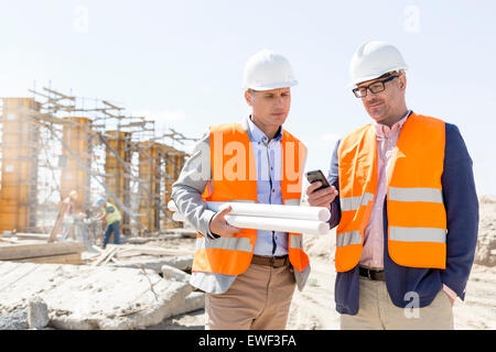 Männliche Ingenieure mit Handy auf Baustelle gegen klarer Himmel Stockfoto