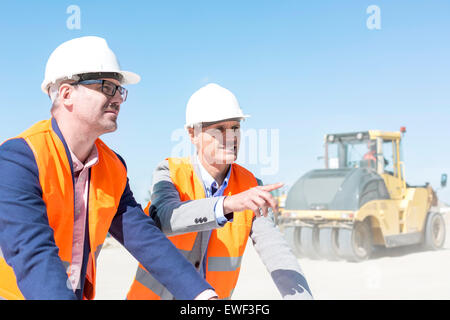 Vorgesetzten erklären Plan an Kollegen bei der Baustelle gegen klaren Himmel Stockfoto