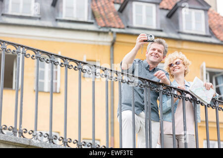 Glückliches Ehepaar mittleren Alters nehmen Selfie durch Digitalkamera gegen Gebäude Stockfoto