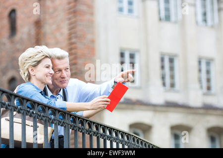 Lächelnd Mann mittleren Alters zeigen etwas auf eine Frau mit Reiseführer in Stadt Stockfoto