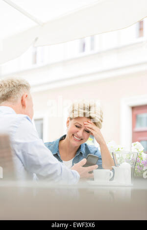 Glückliche Frau mittleren Alters mit Mobiltelefon mit Mann am Straßencafé Stockfoto