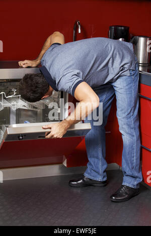 Junger Mann, Blick auf Geschirrspüler Stockfoto