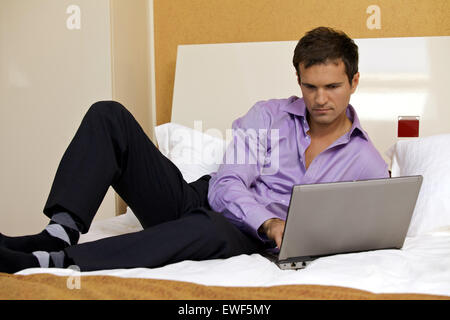 Junger Mann mit Laptop am Bett Stockfoto