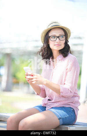 Frau auf der Suche nach Handy auf Bank im Freien halten Stockfoto