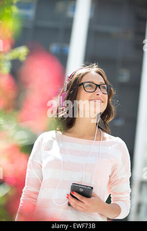 Lächelnde junge Frau wegsehen beim hören von Musik im freien Stockfoto