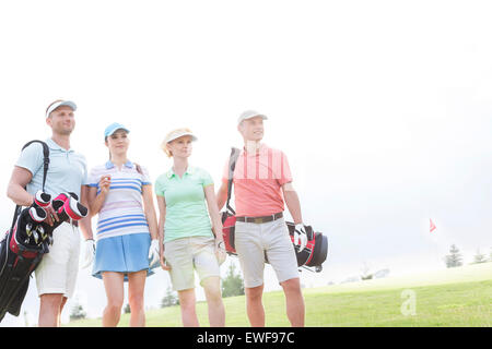 Männliche und weibliche Freunde am Golfplatz gegen klaren Himmel stehen Stockfoto