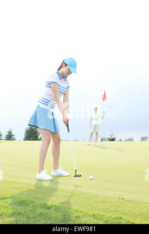 Frau spielt Golf mit Freundin hält Fahne gegen Himmel Stockfoto