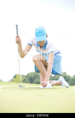 Junge Frau platzieren Ball kniend am Golfplatz Stockfoto