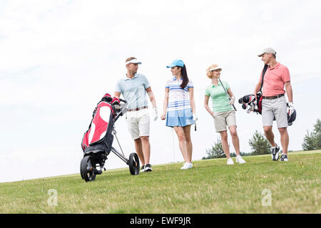 Freunde sprechen während des Gehens auf Golfplatz gegen klaren Himmel Stockfoto