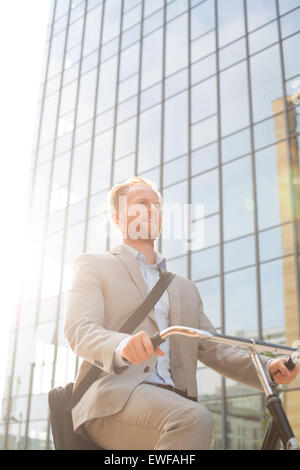 Niedrigen Winkel Ansicht der Geschäftsmann Reiten Fahrrad außerhalb Bürogebäude am sonnigen Tag Stockfoto