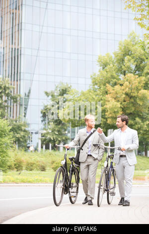 Geschäftsleute sprechen während des Gehens mit Fahrrädern auf Straße Stockfoto