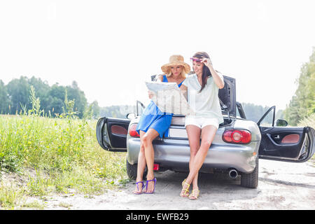 Freundinnen, die Karte zu lesen, während stützte sich auf Cabrio Stockfoto