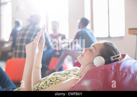 Lässige Geschäftsfrau entspannend mit Kopfhörer und digital-Tablette auf Bohnenbeutelstuhl Stockfoto