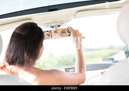 Frau, die Anpassung der Rückspiegel mit Handy im Auto Stockfoto