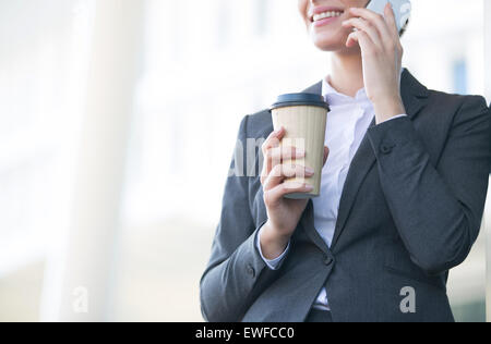 Mittelteil der Geschäftsfrau mit Handy halten Sie Einweg-Cup im freien Stockfoto