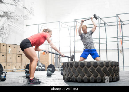 Mann und Frau schlagen Reifen mit Vorschlaghammer in Crossfit gym Stockfoto