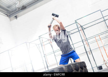 Mann schlägt Reifen mit Vorschlaghammer in Crossfit gym Stockfoto