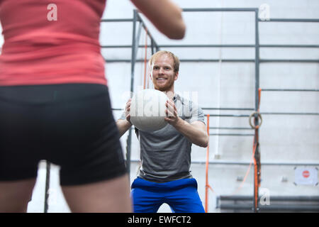 Glücklicher Mann wirft Medizinball in Richtung Frau in Crossfit gym Stockfoto