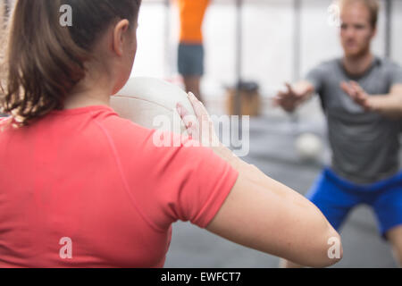 Rückansicht des Frau wirft Medizinball in Richtung Mann in Crossfit gym Stockfoto