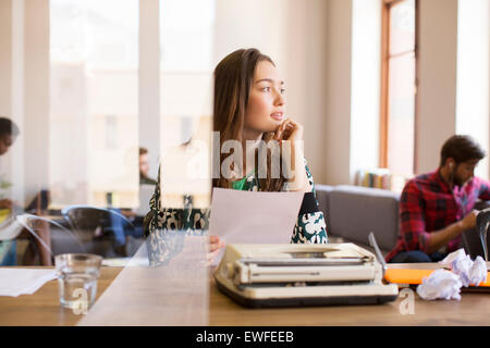 Nachdenklich kreative Geschäftsfrau mit Papierkram an Schreibmaschine im Büro Stockfoto