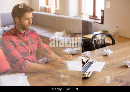 Kreativer Schriftsteller mit Kopfhörern mit Schreibmaschine im Büro Stockfoto