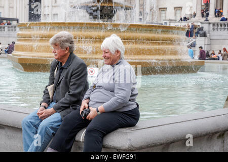 Gerne älteres Paar sitzt auf dem Brunnen am Trafalgar Square, London England Vereinigtes Königreich UK Stockfoto