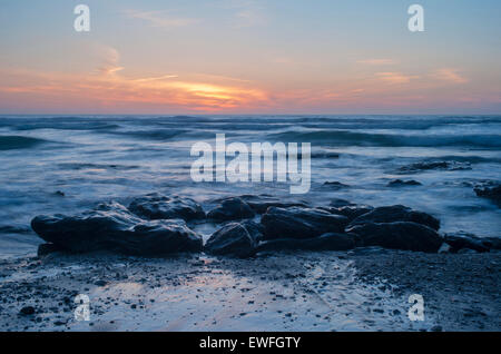 Felsen am Strand mit Wellen, die sich im rollenden bei Sonnenuntergang. Stockfoto