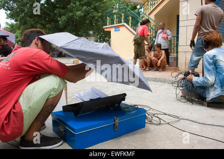 Ein Mann ist die Einrichtung eines Regenschirms wie ein Filmteam eine Szene in einem buddhistischen Tempel in Phnom Penh, Kambodscha schießt. Stockfoto