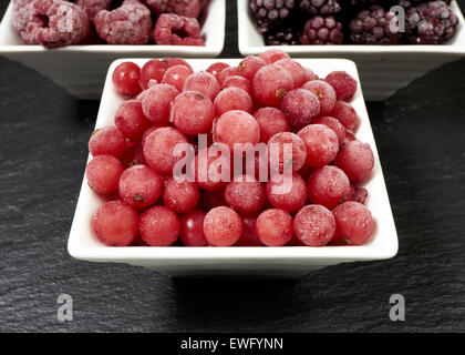 Nahaufnahme von drei kleinen Porzellangeschirr mit gefrorenen Himbeeren, Johannisbeeren und Brombeeren auf dem Schiefer Tablett Stockfoto