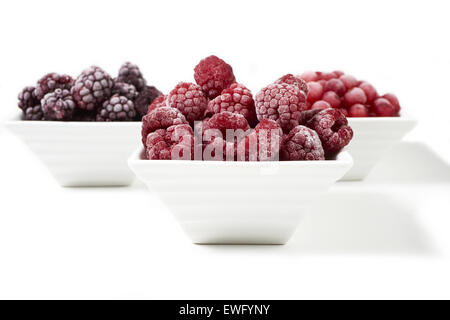 Drei kleine Porzellangeschirr mit gefrorenen Himbeeren, Johannisbeeren und Brombeeren auf weißem Hintergrund Stockfoto