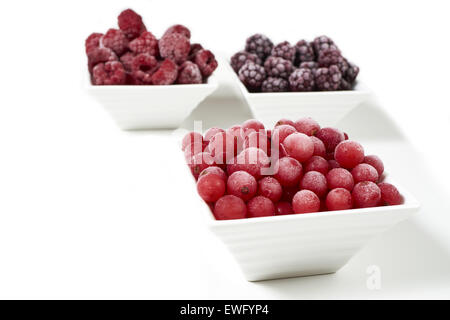 Drei kleine Porzellangeschirr mit gefrorenen Himbeeren, Johannisbeeren und Brombeeren auf weißem Hintergrund Stockfoto