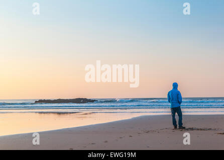 Einsame person, die auf den Strand bei Sonnenuntergang mit Blick auf den Ozean. Stockfoto