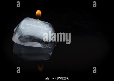 Eine Nahaufnahme von einer brennenden Kerze Docht steckte in einen Eiswürfel auf einem schwarzen Hintergrund mit Reflexion. Stockfoto