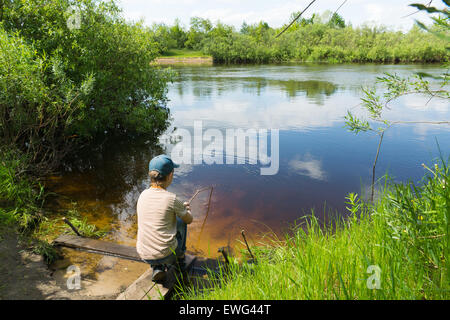 der junge in einer Kappe fängt Fische im Fluss auf eine selbstgebaute Rute Stockfoto