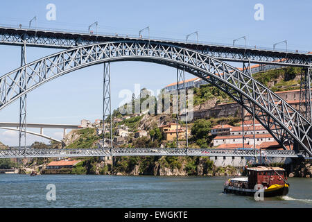 Dom Luis I Brücke, die obere Ebene ein Gehweg und eine Metro ist Linie und Autos auf der unteren Ebene trainieren. Lastkähne nehmen Touristen auf Kreuzfahrten auf dem Douro. Porto, Portugal. Stockfoto