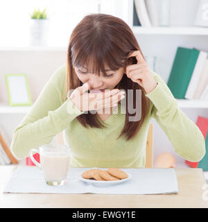 Asiatische Frau Übelkeit während Frühstück, Milch und Kekse auf Esstisch. Junges Mädchen im Haus Lebensweise zu Hause. Stockfoto