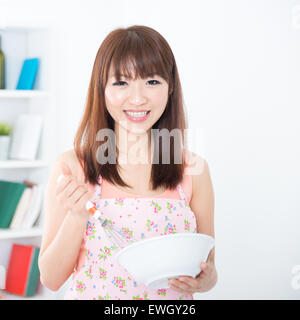 Glückliche asiatische Hausfrau mit Schürze, Zubereitung von Speisen, mit manuellen Ei Mixer und Schüssel. Junge Frau, die Zuhause Leben Lifestyle zu Hause. Stockfoto