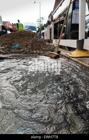 Gebrochenen / platzen Wasserleitung Rohr undicht kann Wasser austreten und entstehen durch die Straße & fließen in die Gosse in / Straße. UK Stockfoto