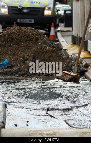 Gebrochenen / platzen Wasserleitung Rohr undicht kann Wasser austreten und entstehen durch die Straße & fließen in die Gosse in / Straße. UK Stockfoto