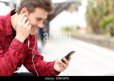 Musikhören mit Ohrhörern über ein Smartphone beim Mann wartet in einem Bahnhof Stockfoto