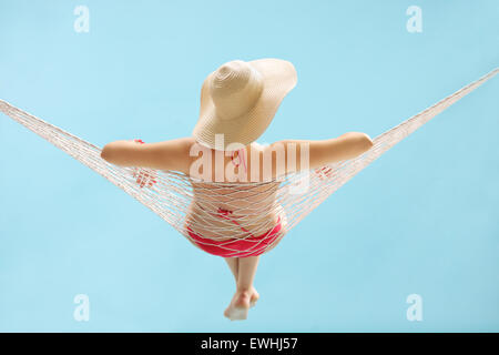 Hintere Ansicht Studioaufnahme eines jungen Mädchens mit einem stylischen Hut liegen in der Hängematte auf blauem Hintergrund Stockfoto