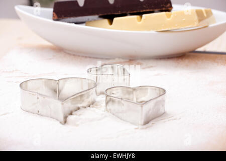 Ausstechformen und weißer und dunkler Kuvertüre Schokolade auf bemehlten Backblech mat Stockfoto