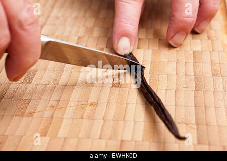 Kratzen Sie Vanillemark aus Pod mit einem Messer auf einem Bambus-Schneidebrett aus Stockfoto