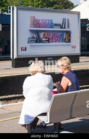 Zwei weibliche Passagiere saßen wartend und im Gespräch mit der Box-Sets, die Poster bei Southampton Central Station in aller Munde ist Stockfoto