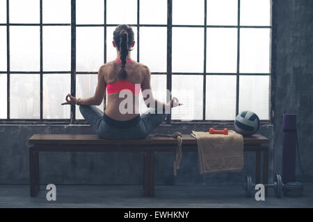 Wie die Stadt unten hastet, sitzt Fit, sportliche Frau still meditieren im Lotussitz auf einer Holzbank. Stockfoto