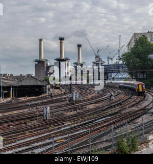 Zwei Züge auf einer gekrümmten Bahn verfolgen Ansatz Victoria Station mit der dramatischen Battersea Power Station renoviert Stockfoto