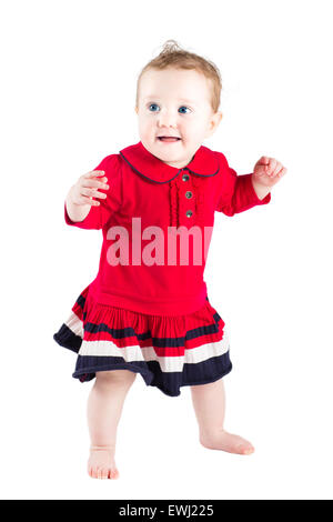 Schöne Mädchen in einem roten Kleid machen ihre ersten Schritte, isoliert auf weiss Stockfoto